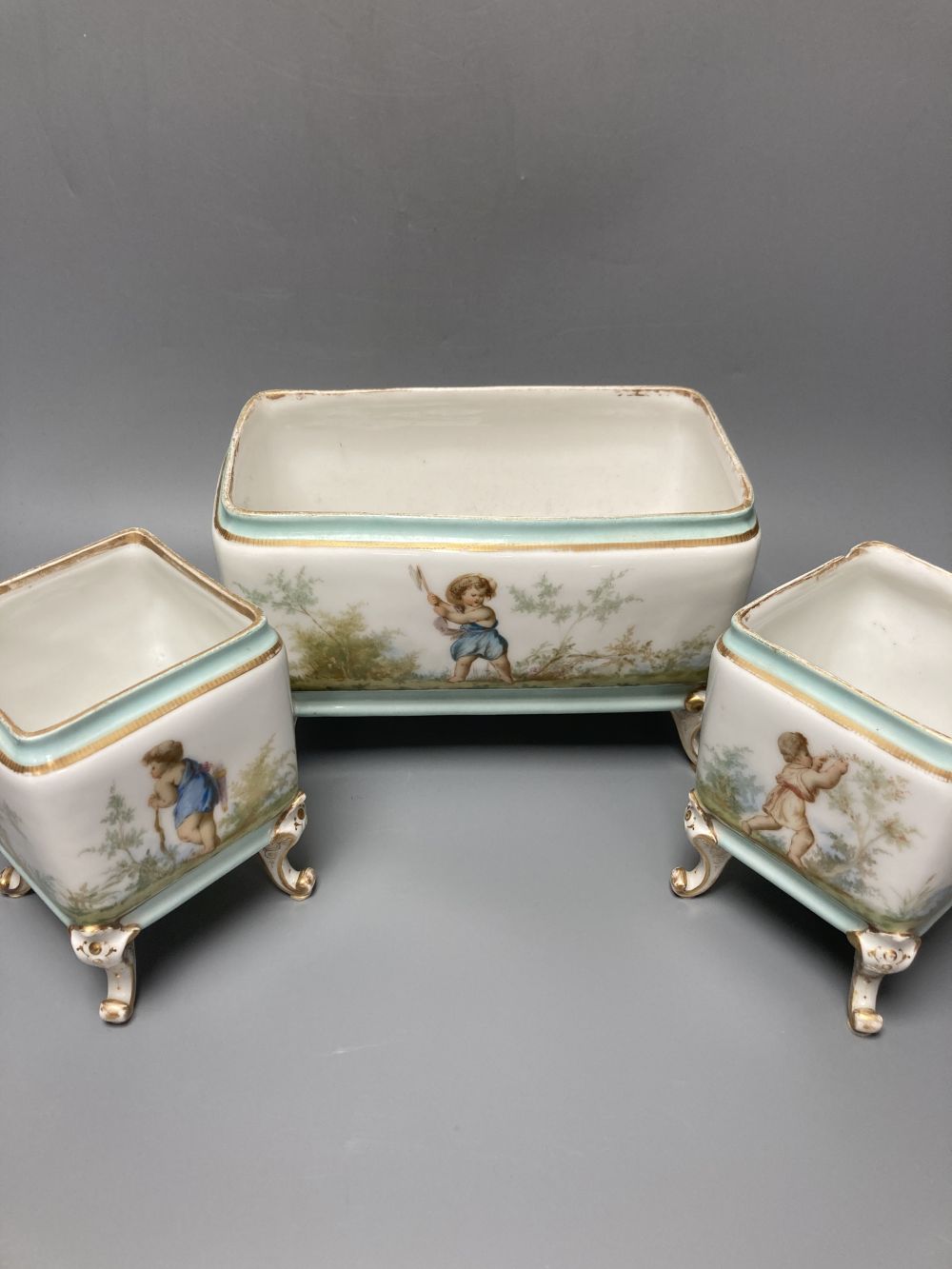 A set of three 19th century French porcelain jardinieres, painted with classical children playing, tallest 14.5cm width 22cm